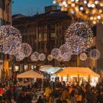 Mercatino di Natale illuminato con bancarelle e decorazioni festive in una piazza italiana.